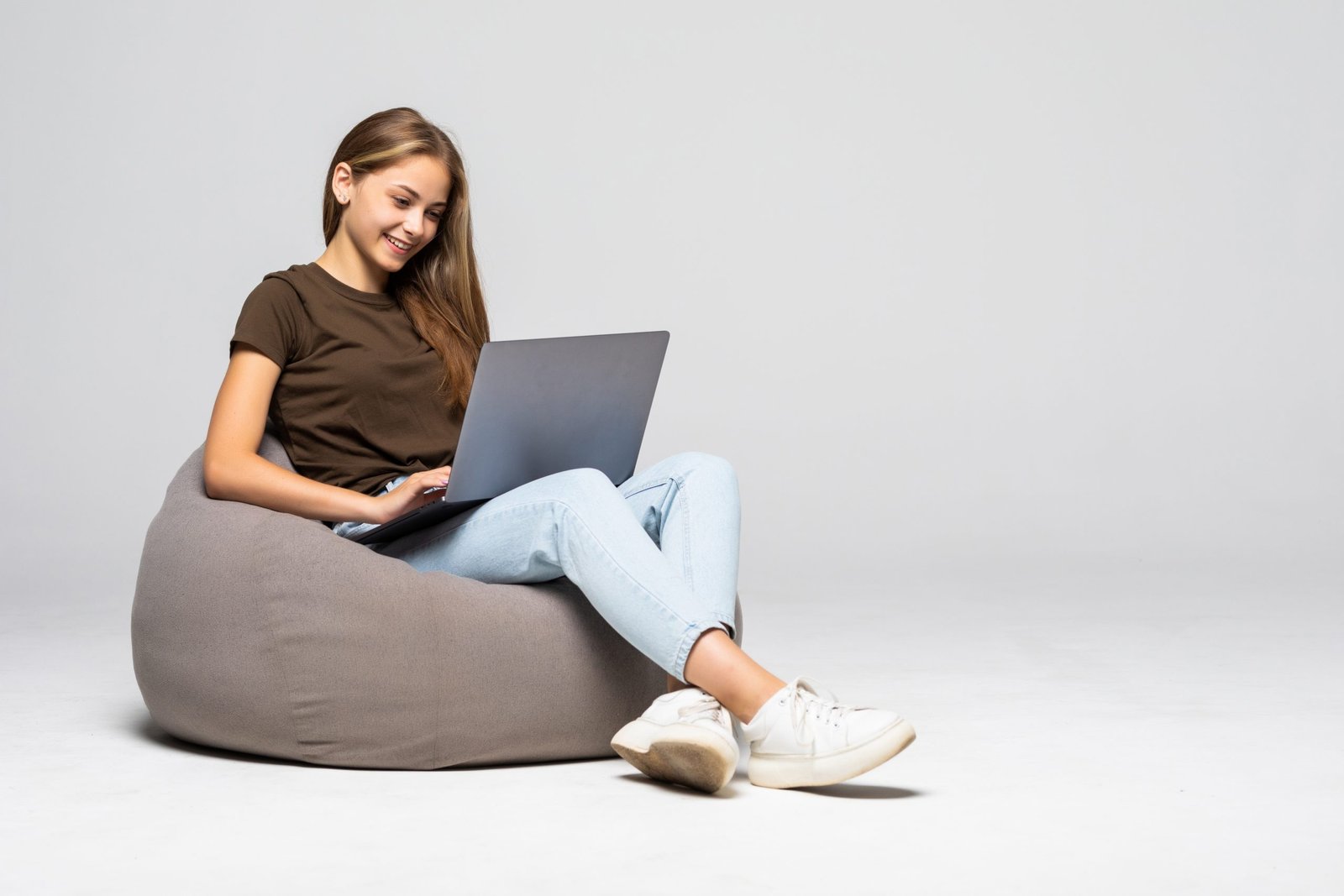 happy young woman sitting floor using laptop gray wall